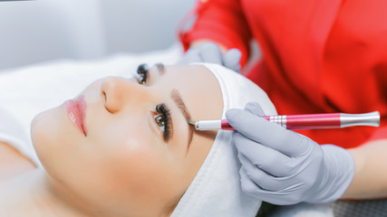 Naklejka premium Beautiful young girl with long eyelashes tweezing her eyebrows in a beauty salon. Eyebrow Correction. Beauty Concept. Permanent Makeup. Microblading brow. Beautician Doing brows Tattooing.