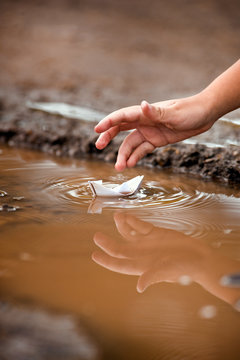 Close up of little boy's hand playing with paper boat in puddle.