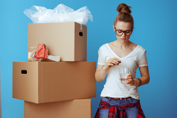 stressed woman near cardboard box drinking sedative on blue