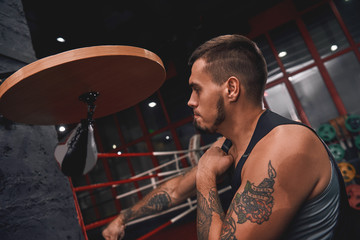 New champion. Close-up of muscular tattooed boxer in sports clothing hitting punching speed bag...