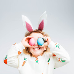Studio shot of a happy little girl wearing bunny ears and holding up a colorful Easter egg in front...