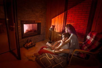 Lovers reading a book by the fireplace. Evening leisure couples. Rest around the fireplace. Cozy home. Romantic atmosphere.