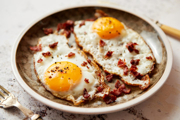 Two fresh fried eggs with crunchy crisp bacon served on rustic plate