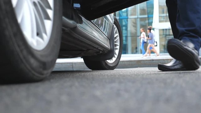 Businessman opens and holds door of car for beautiful young woman. Slim legs of businesswoman in shoes on high heels getting out of auto. Close up Slow motion Low angle view