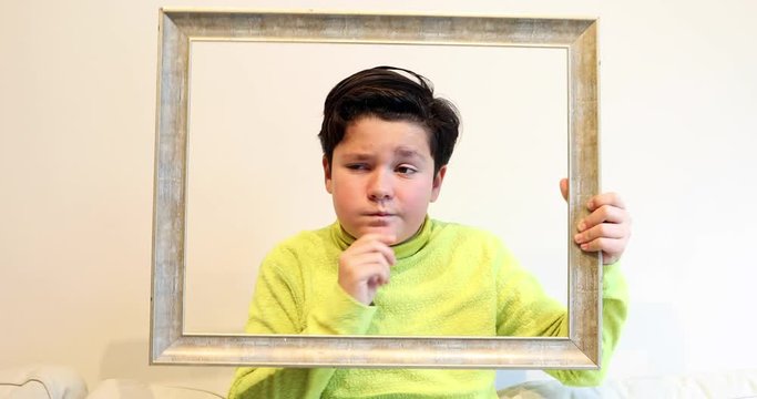 Portrait of a handsome young boy  looking through emty frame and making silly faces to a camera