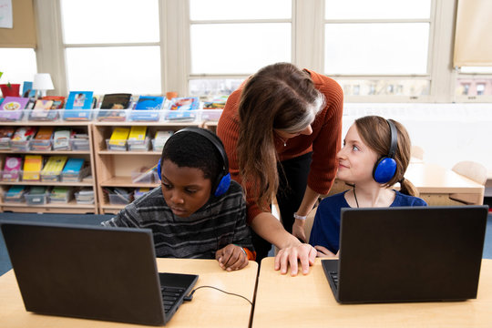 Teacher helping students with laptop computers