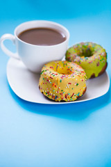 Two colored donuts on a plate with a cup of coffee. Yellow and Green Donut on a blue background. Dessert
