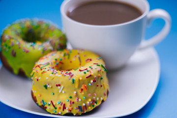 Two colored donuts on a plate with a cup of coffee. Yellow and Green Donut on a blue background. Dessert
