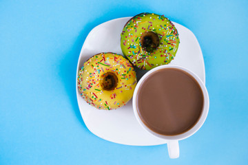 Two colored donuts on a plate with a cup of coffee. Yellow and Green Donut on a blue background. Dessert