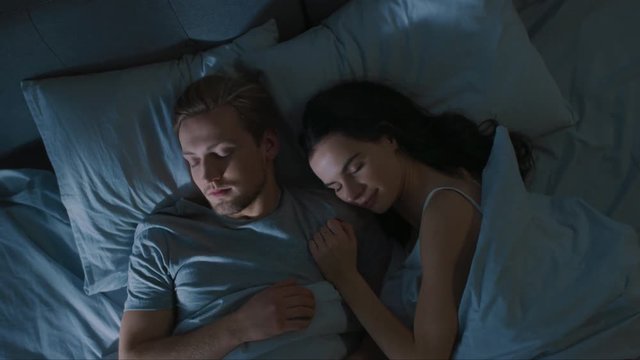 Top View Bed at Night: Attractive young Couple Sleeping Together, Holding Each other in Arms, Embracing. First Rays of Morning Sun Illuminate Room Trough the Window
