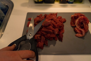 Beautiful Red Raw meat getting cut by scissors in kitchen cooking plate.
