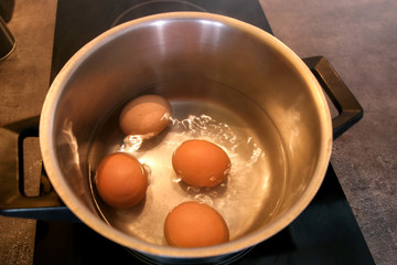 Top view of boiling organic eggs in metal pot into saucepan on electric stove in kitchen. Four chicken eggs in pot with boiling water. Boiling village eggs in hot water. Eggs cooked, high temperature.