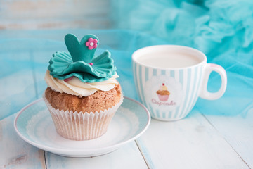 Cupcake and a mug on turquoise background. Bright blue wooden table