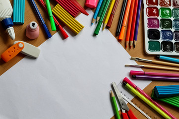 Top view on table with blank sheet of paper. Back to school concept with space for text. Color paints with paint brushes, pencils and plasticine. Kids painting concept. Children art.