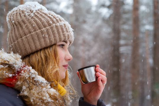 girl holds in her hand a cup of tea (thermos cap) outdoors on a frosty day