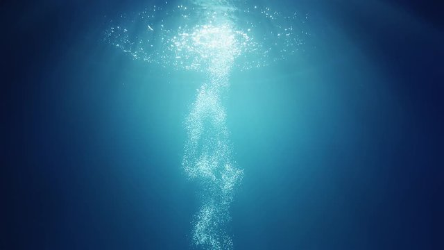 Sun light beams shining from above coming through the deep crystal clear blue water causing a beautiful water lighting reflections curtain with air bubbles rising up to the surface