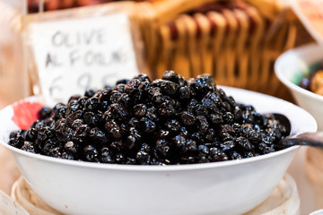 Black olives many closeup in Florence Italy central market in bowl with sign and spoon scoop