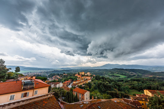 Chiusi evening in Umbria, Italy with rooftop houses on mountain countryside rolling hills and colorful picturesque cityscape with storm grey dark clouds
