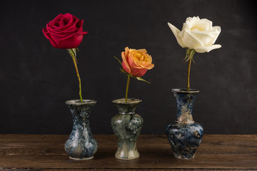 Three small marble vases with different roses on black background