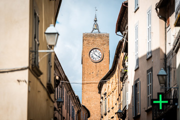 Fototapeta na wymiar Orvieto, Italy Italian outdoor empty street in Umbria historic city town village road narrow alley with orange walls green pharmacy cross sign and church clock tower