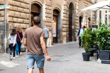 Orvieto, Italy Italian outdoor street in Umbria historic city town village cobblestone road alley with people tourists young man back walking in summer
