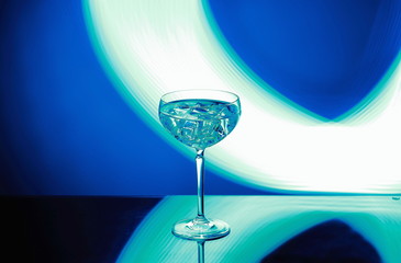 Beautiful view of alcohol drink with ice cubes in crystal glass on colorful background. 