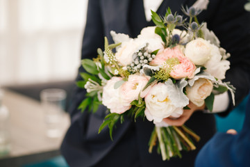 Groom in classy suit stands with a wedding bouquet