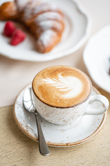 Coffee cappuccino with croissant on white plate in restaurant. Light morning Breakfast, fresh warm pastries and raspberries