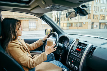 young pretty woman driving car while drinking cup of coffee