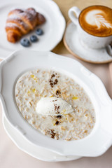 Bowl of breakfast oatmeal with soft Italian cheese and cinnamon. Croissants, coffee and other dishes on the table in the restaurant