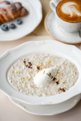 Bowl of breakfast oatmeal with soft Italian cheese and cinnamon. Croissants, coffee and other dishes on the table in the restaurant