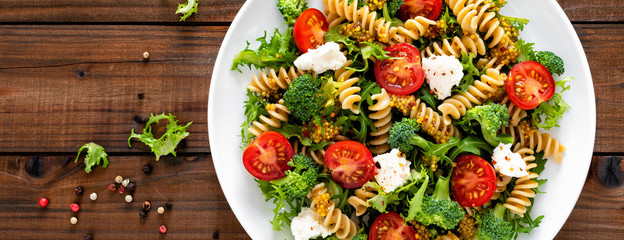 Italian pasta salad with wholegrain fusilli, fresh tomato, cheese, lettuce and broccoli on wooden...