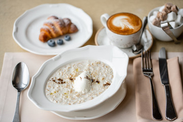 Bowl of breakfast oatmeal with soft Italian cheese and cinnamon. Croissants, coffee and other dishes on the table in the restaurant