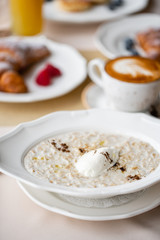 Bowl of breakfast oatmeal with soft Italian cheese and cinnamon. Croissants, coffee and other dishes on the table in the restaurant