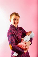 Young dad holds a newborn baby in his arms in the studio on a pink background.