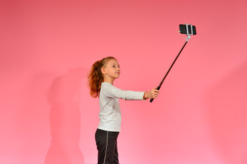A girl takes a selfie on a smartphone in the studio on a pink background.
