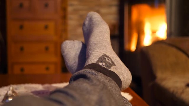 Feet with socks close up with orange bright fire burning in the background warm, relaxed and cozy inside on a winters night