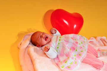 A newborn baby is lying in a pink lullaby on a yellow background with children's toys.