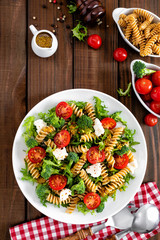 Italian pasta salad with wholegrain fusilli, fresh tomato, cheese, lettuce and broccoli on wooden rustic background. Mediterranean cuisine. Cooking lunch. Healthy diet food. Top view