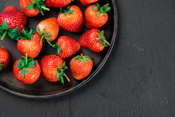 Fresh strawberry in wrought plate on  dark board. 