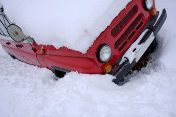 The red car is stuck in the snow after the snowfall.