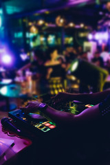 Obraz premium DJ plays live set and mixing music on turntable console at stage in the night club. Disc Jokey Hands on a sound mixer station at club party. DJ mixer controller panel for playing music and partying.