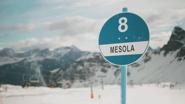 A slope sign swaying in the wind, you can see the Dolomites mountains in the background.