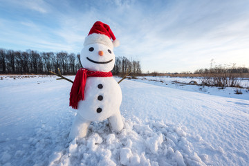 Funny snowman in santa hat and red scalf on snowy field. Christmass and New Year background