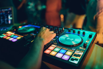 Obraz premium DJ plays live set and mixing music on turntable console at stage in the night club. Disc Jokey Hands on a sound mixer station at club party. DJ mixer controller panel for playing music and partying.