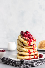 Stack of pancakes with cherry sauce and chocolate on a white plate. Grey concrete background. Copy space. Breakfast.