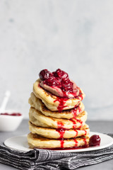 Stack of pancakes with cherry sauce and chocolate on a white plate. Grey concrete background. Copy space. Breakfast.