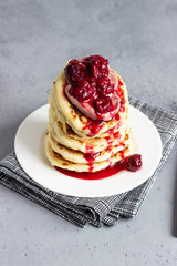 Stack of pancakes with cherry sauce and chocolate on a white plate. Grey concrete background. Copy space. Breakfast.