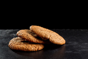 Wholegrain oatmeal cookies on black slate background.
