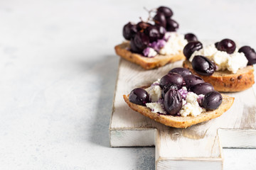 Bruschetta with ricotta or cream cheese and baked grapes on a light wooden cutting board.